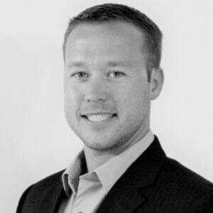 Joshua Kuphal Headshot Monochrome photo of Josh wearing a dark suit jacket over a light colored button-up shirt