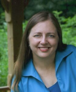 Kimberly Paarlberg Headshot Kim is wearing a blue button-up shirt open over a darker blue top