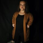 Kori is wearing a brown cardigan over a black outfit