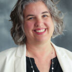 Marsha is wearing a white blazer over a black top