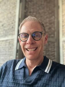 Mark is wearing a blue textured polo shirt with white stripes along the edges of the collar.