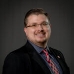 RandyWallace Randy is smiling and wearing glasses and a dark suit.