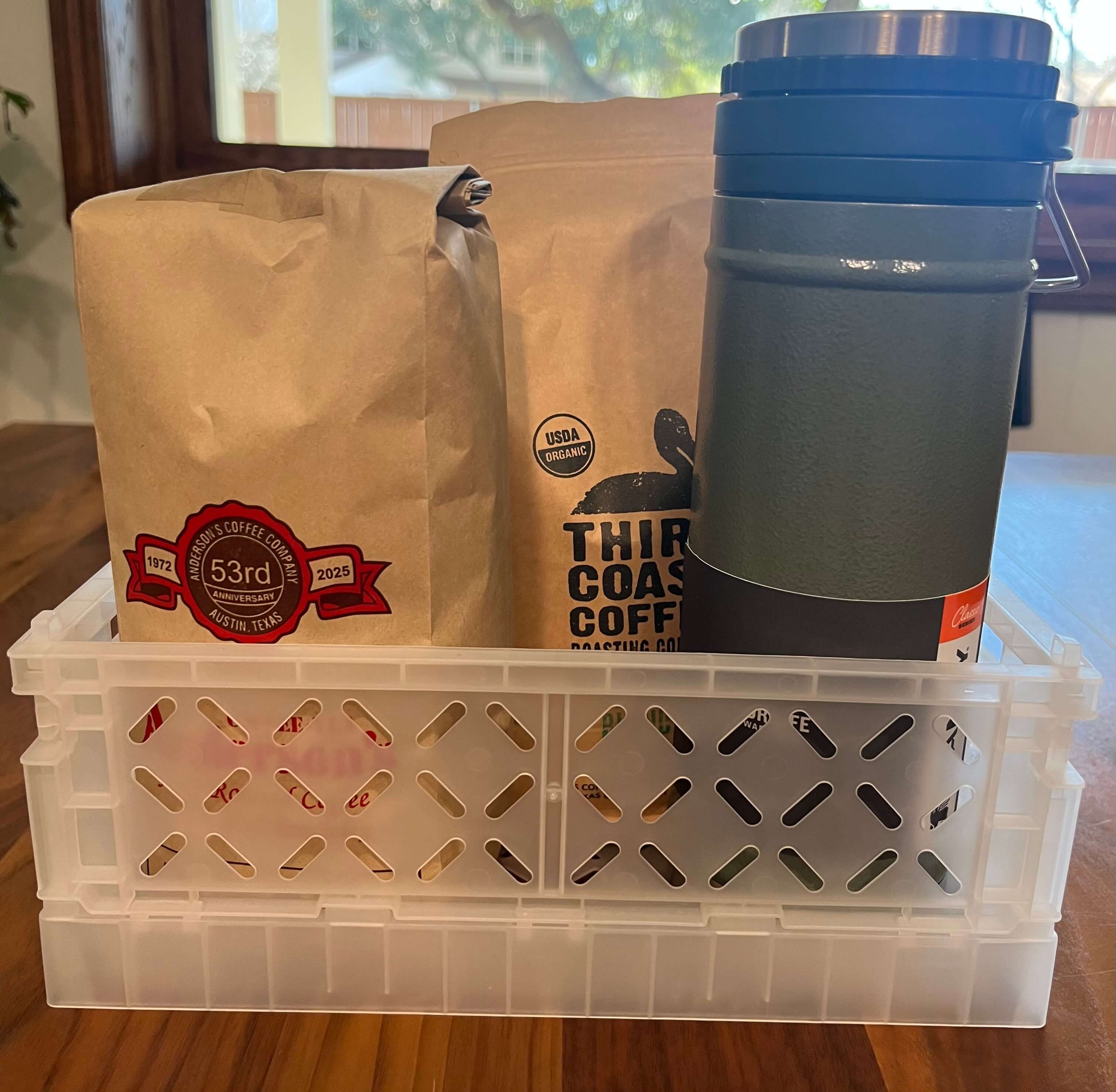 A basket with a french press mug and two bags of coffee