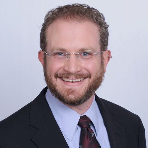 Josh Schorr Heaadshot Josh is wearing a suit and tie and smiling brightly at the camera