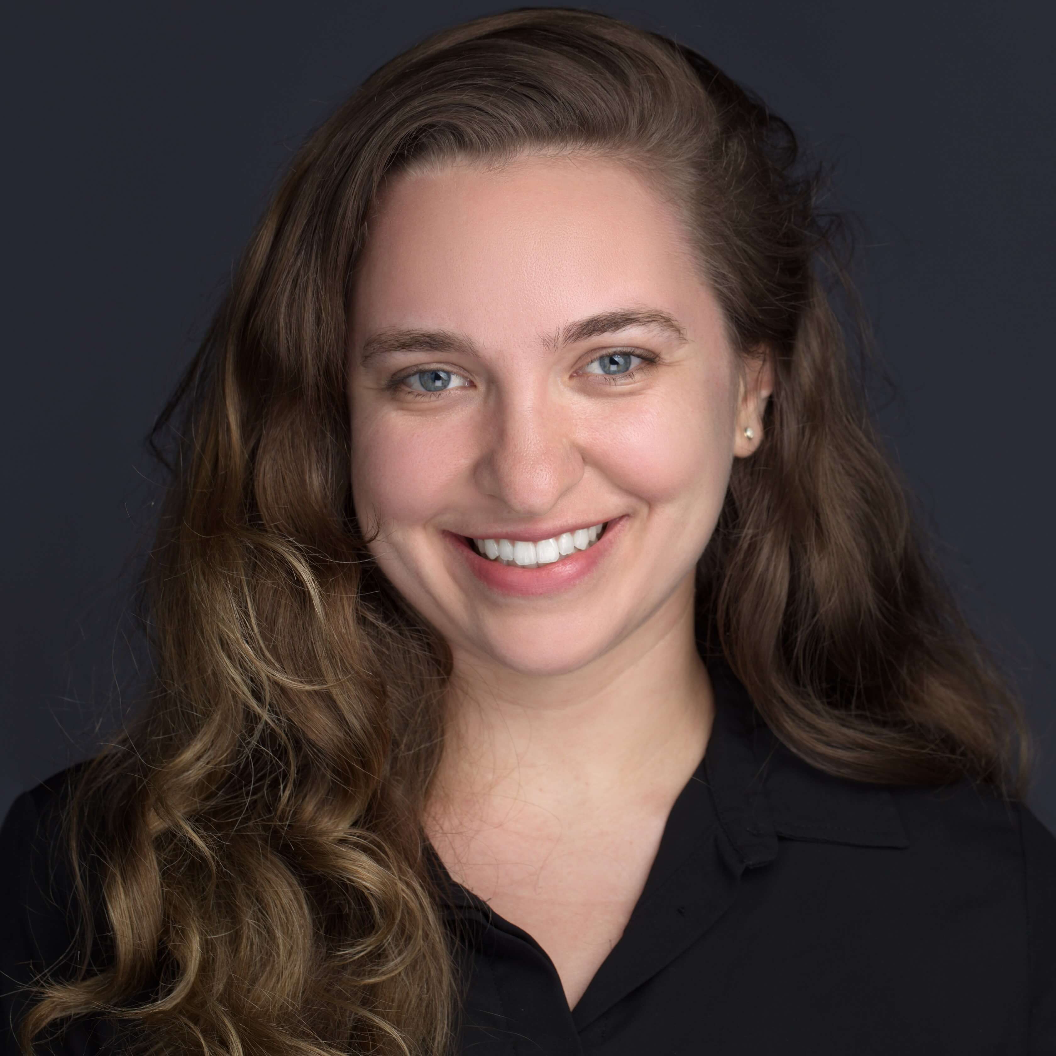 Luísa has long wavy, dark hair and is wearing a dark button up shirt