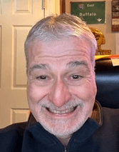 Dominic has white hair and is smiling brightly at the camera.