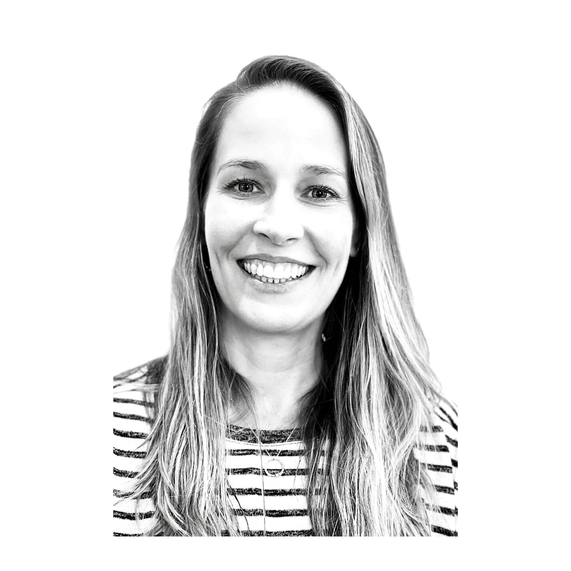 Black and white headshot of Angela Shapiro smiling, featuring long hair and a striped shirt against a plain white background.