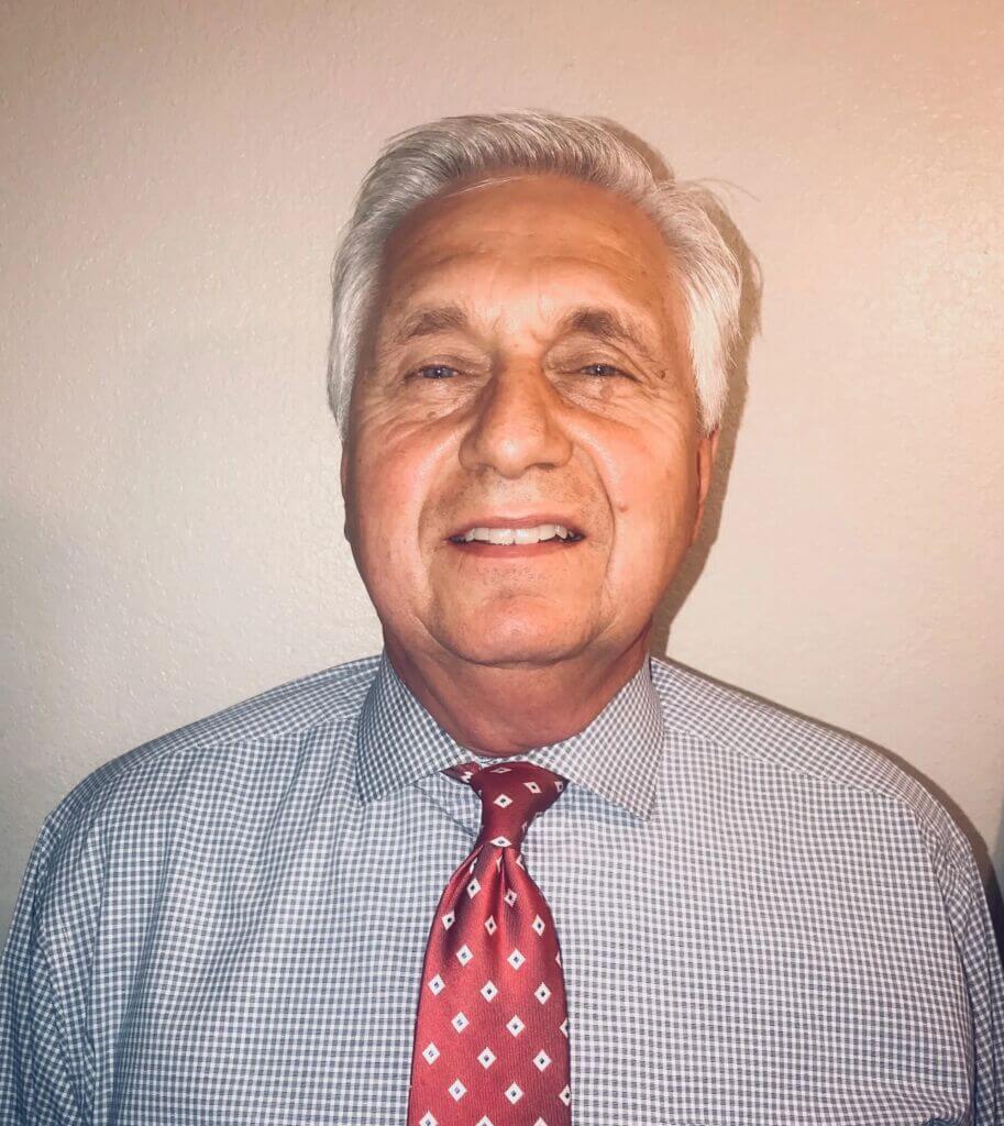 Headshot of Thomas smiling, wearing a blue and white patterned button-down shirt and a patterned red tie