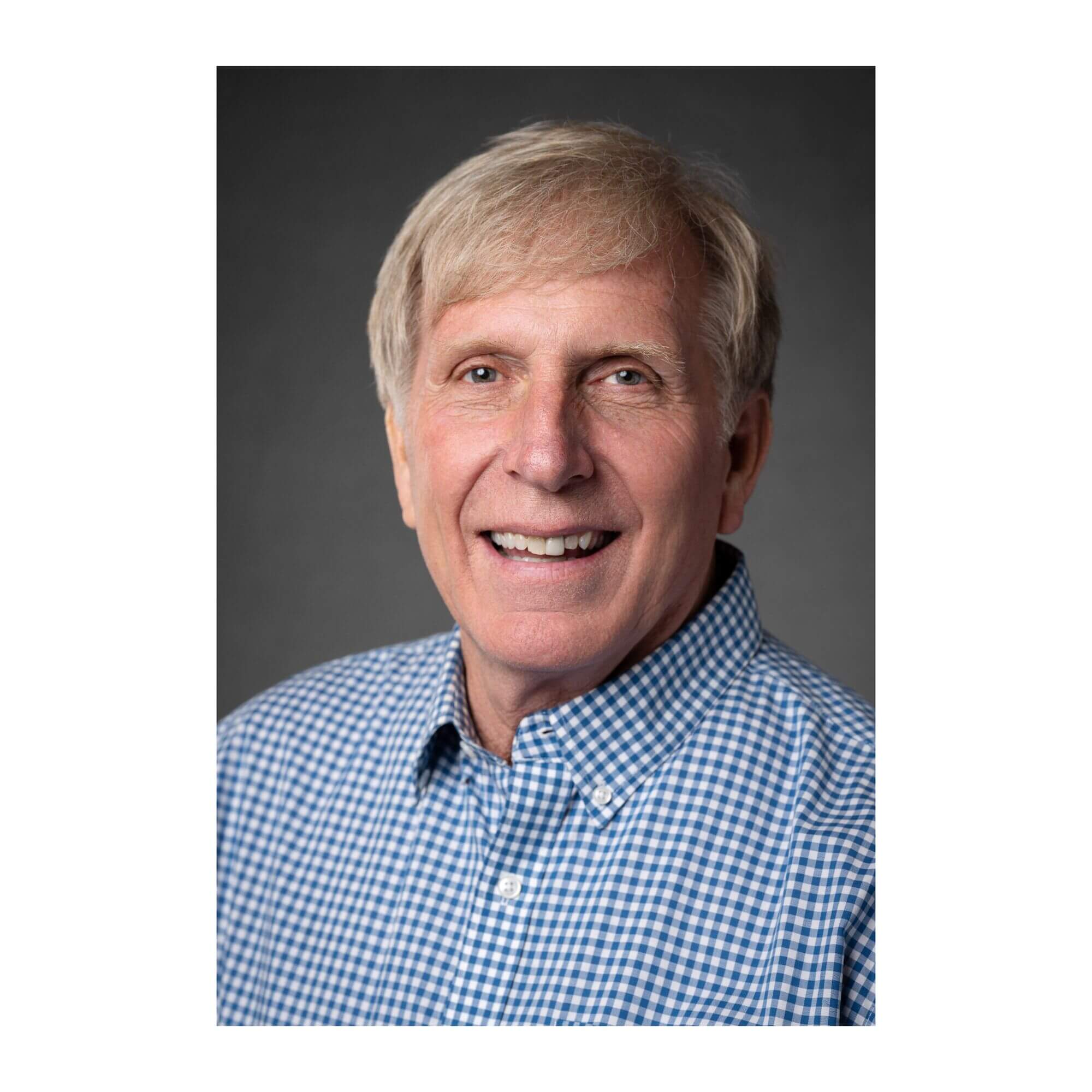 Bill Botten Headshot of Bill Botten smiling, wearing a blue and white gingham collared shirt against a neutral grey background.