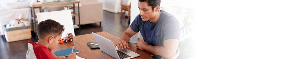 father working at kitchen table while does homework across the table