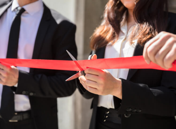 Photo of a woman cutting a red ribbon at a ribbon cutting