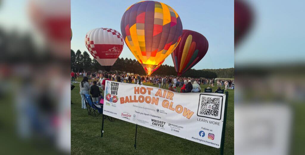 Hot Air Balloon Glow supporter recognition banner displayed in front of illuminated grounded balloons during Berry Dairy Days in Burlington, Washington.