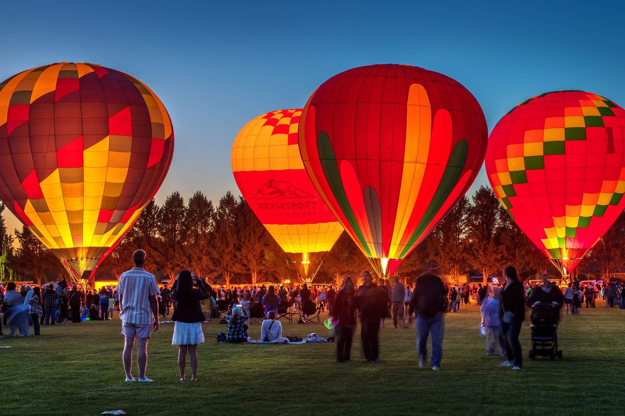 Festivalgoers gather around glowing hot air balloons at blue hour during Berry Dairy Days in Burlington, Washington.