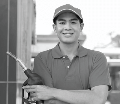 A smiling man with crossed arms holding a gas nozzle