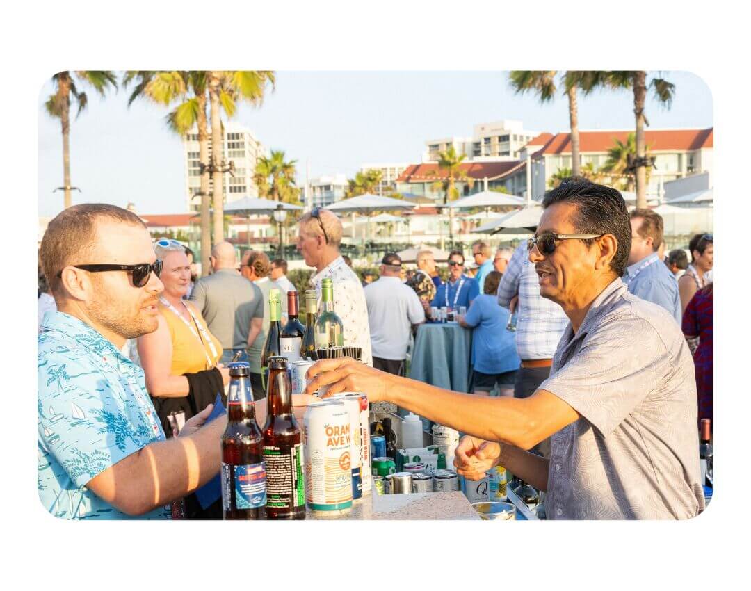 2 men in a crow drinking beer surrounded by palm trees