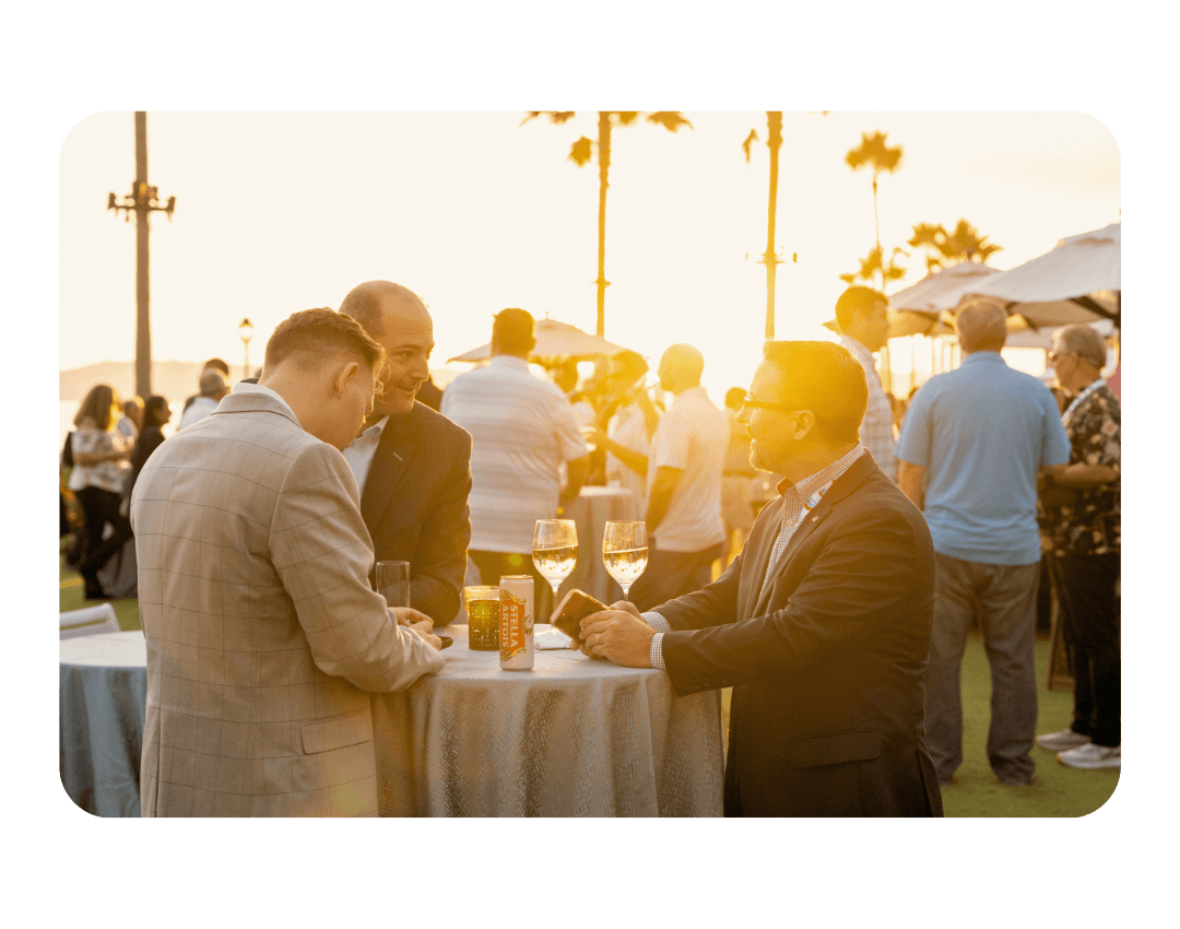 3 men around a table at sunset talking and drinking