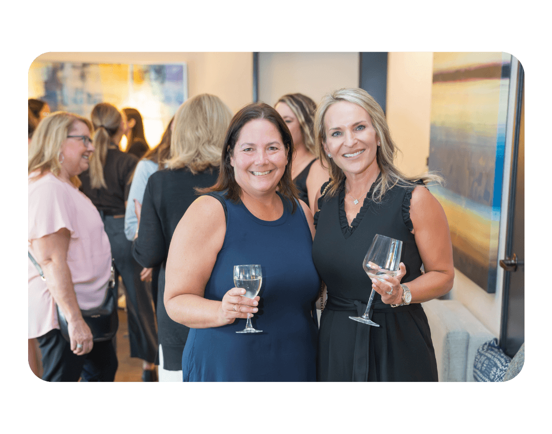 2 women in dresses smiling and holding wine glasses
