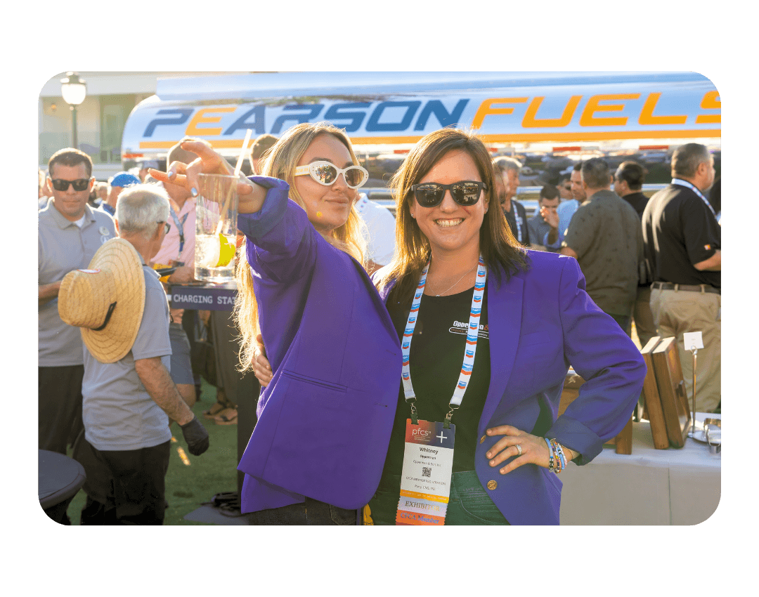 2 women pose with drinks in front of a large tanker truck
