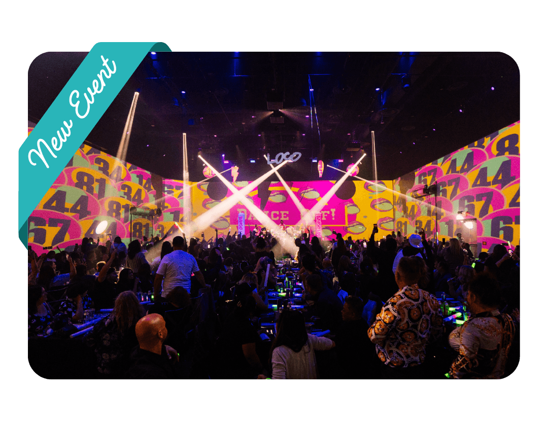 A crowd of people in front of a stage with spotlights and colorful digital stage background