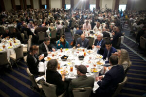 Conference attendees eating lunch in a large hotel ballroom.
