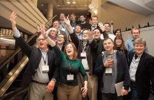 A photo of David Donald with a group of CPI alumni standing on a stairwell in a hotel. Everyone is gesturing to someone out of the frame. It kind of looks like everyone's trying to hail a taxi.