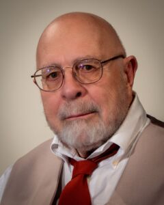 Portrait of Hank Nuwer. Hank is wearing a tan suit and a red tie.
