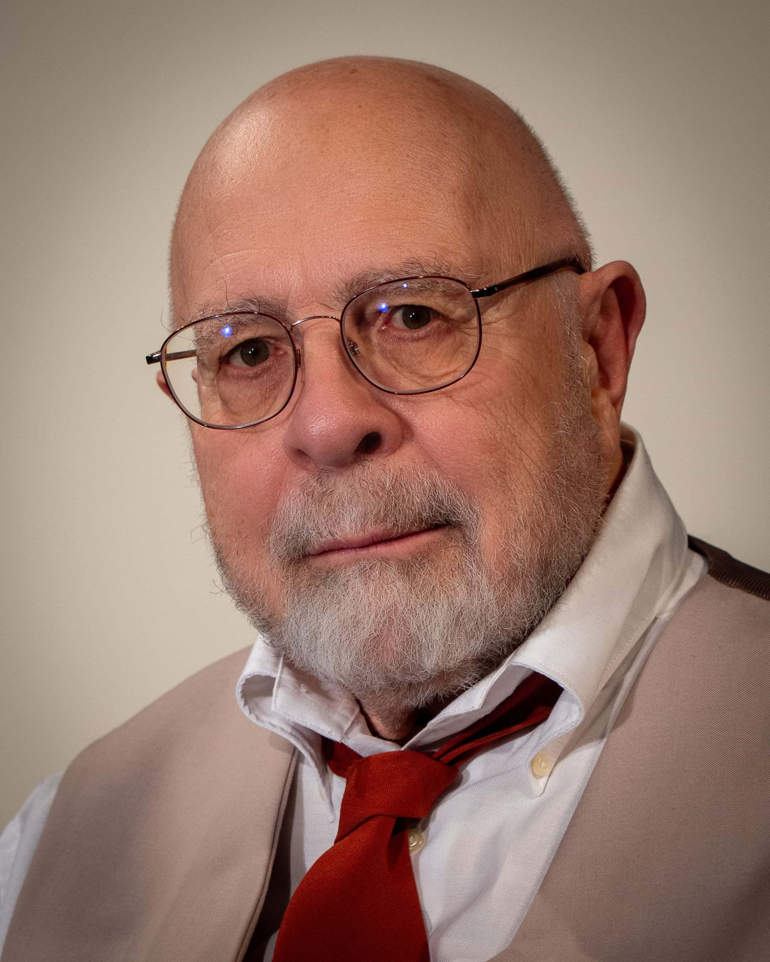 Portrait of Hank Newer. Hank is wearing a tan suit and a red tie.