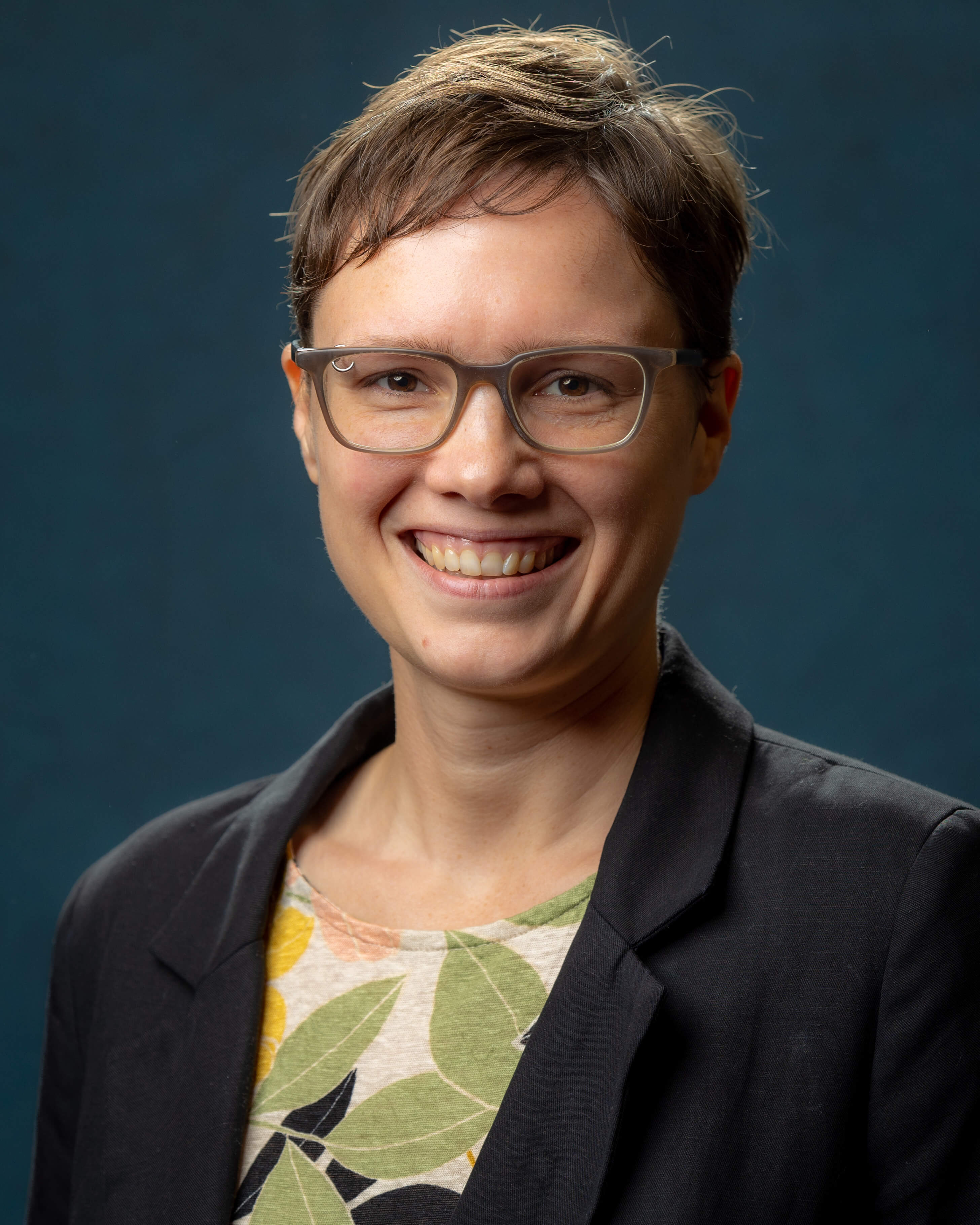 Portrait of Liz Lucas smiling, wearing a blazer against a blue background