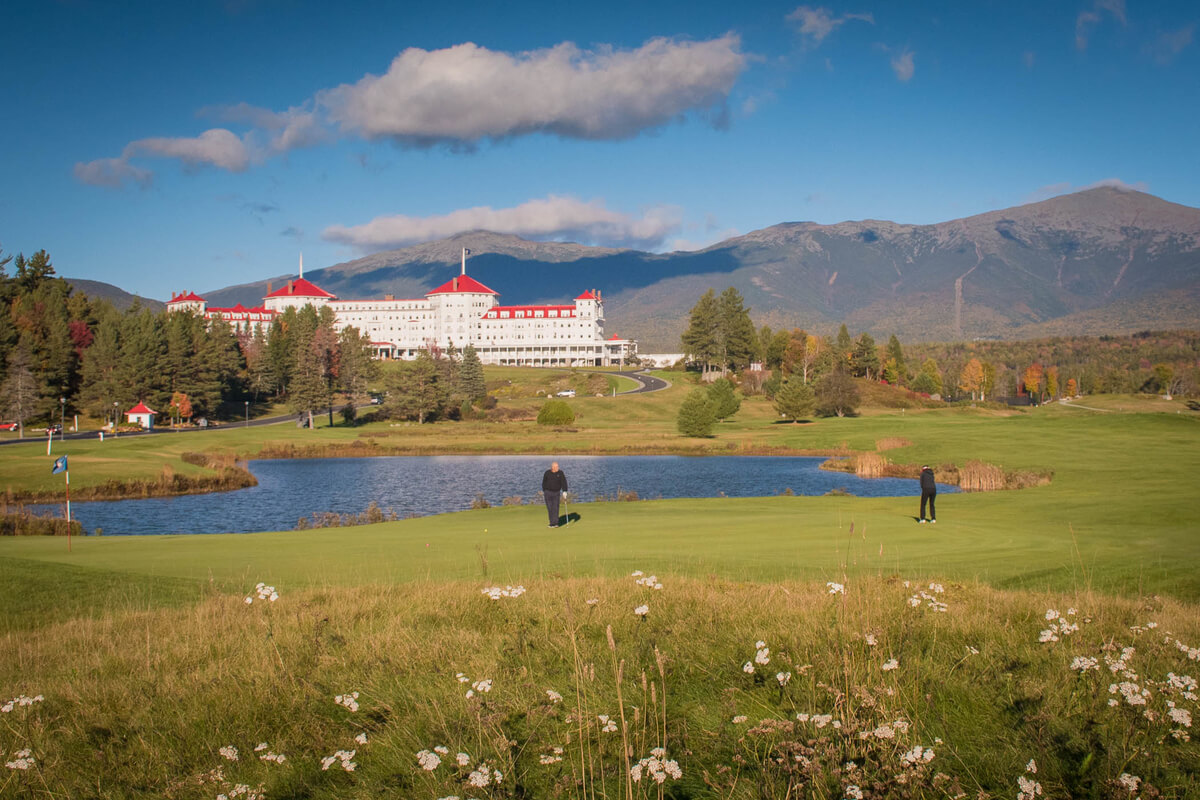 Two golfers on the putting green in front of the Omni Mount Washington Resort.
