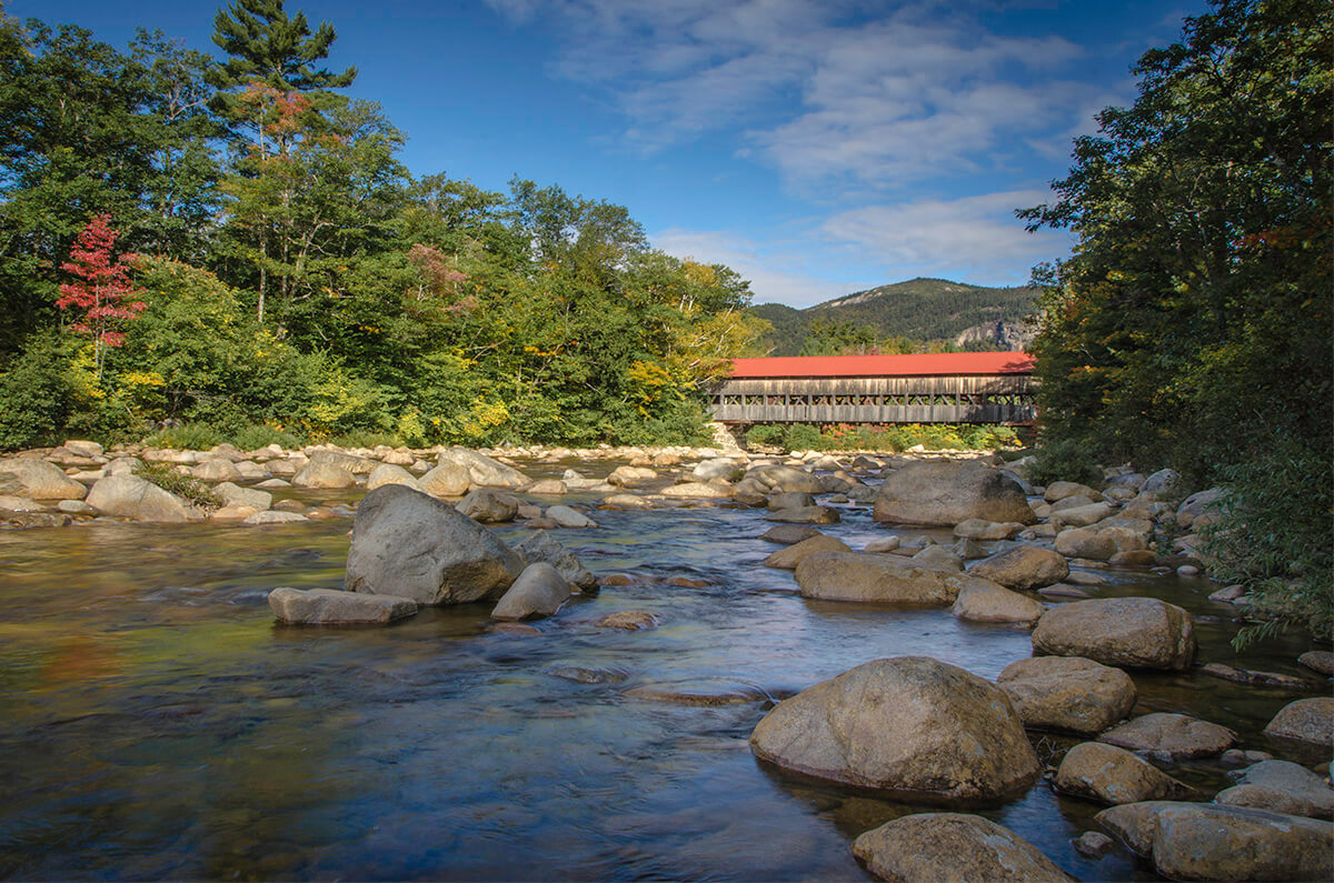 The Albany Covered Bridge in the daytime with mountains in the background.