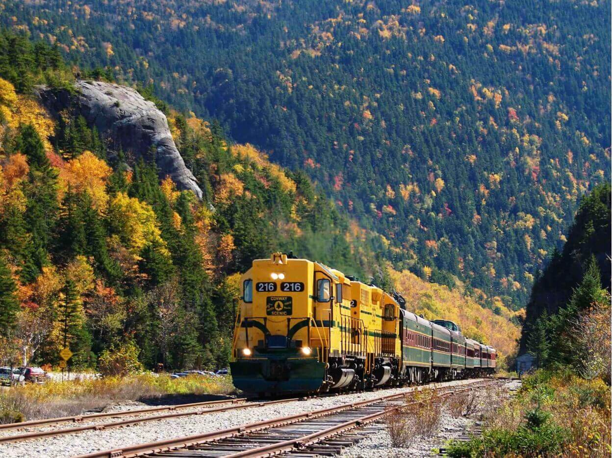 Conway Scenic Railroad going through the White Mountains with foliage around.