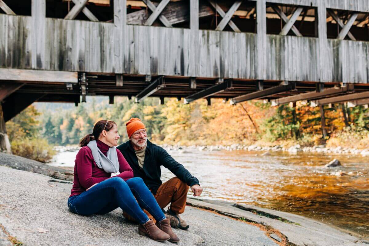 A couple sitting on rocks under a covered bridge in the fall.