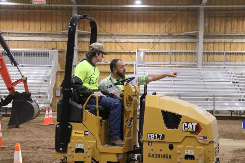 student driving heavy machine with instructor pointing the way