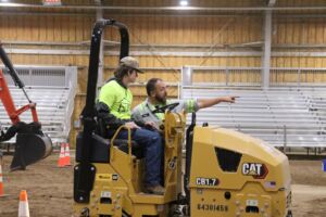 student driving heavy machine with instructor pointing the way