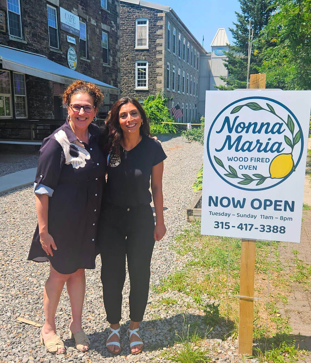 Two Women standing in front of Now Open sign