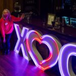 woman next to neon xo sign