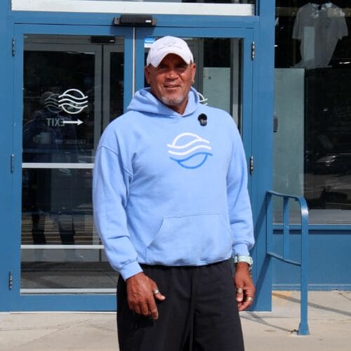 Man in a light blue hoodie and cap standing outside a building entrance