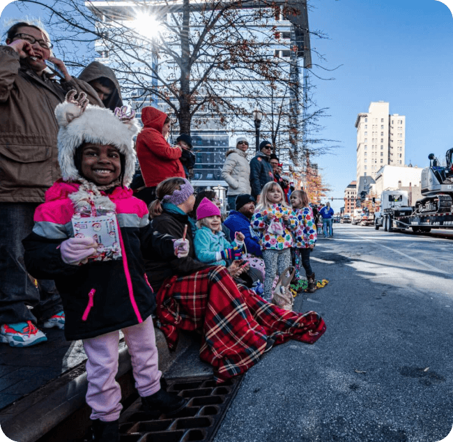 Families lined up along street watching Shop Sip & Celebrate parade