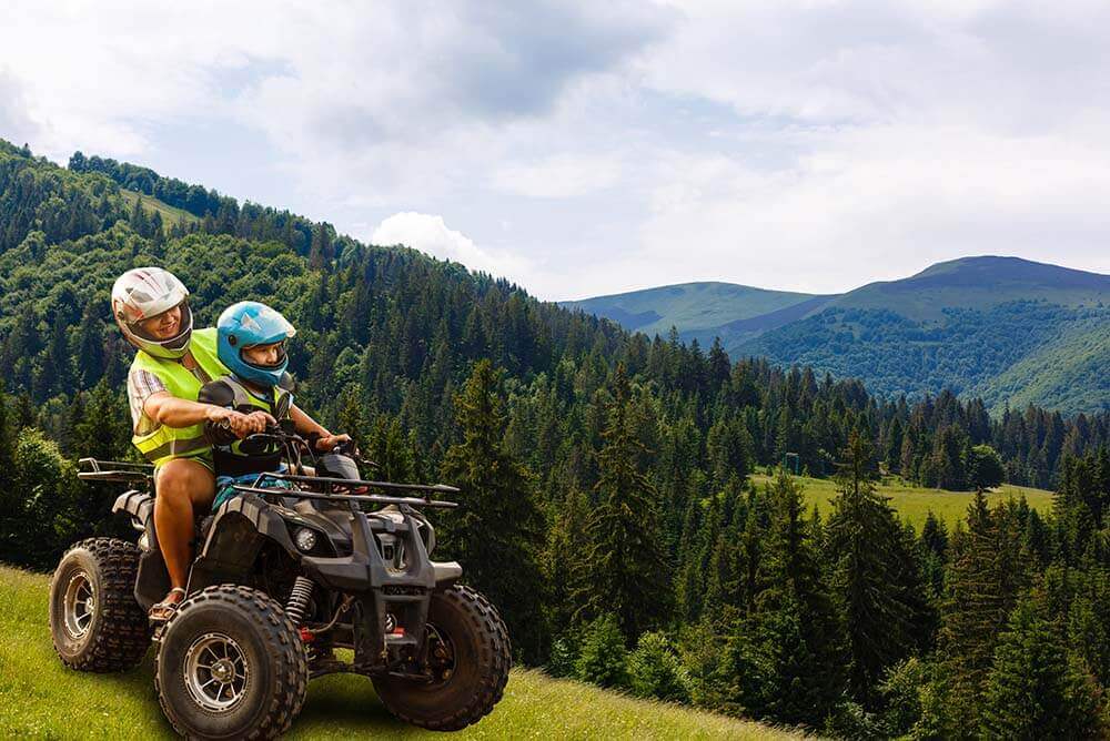 Adult with a kid riding ATV in the mountains