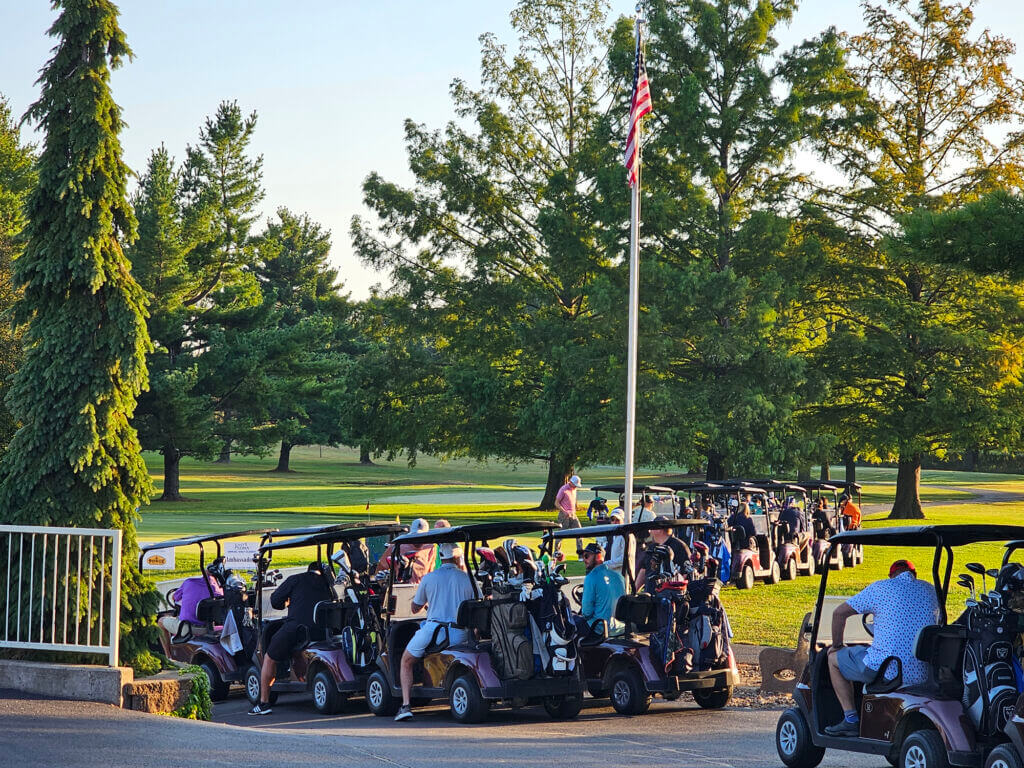 Golf carts lined up along the course with an American flag visible in the background
