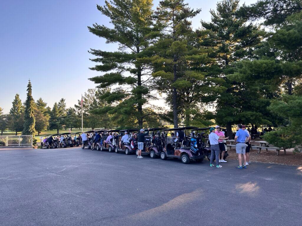 A long row of golf carts lined up on the course with participants gathered nearby