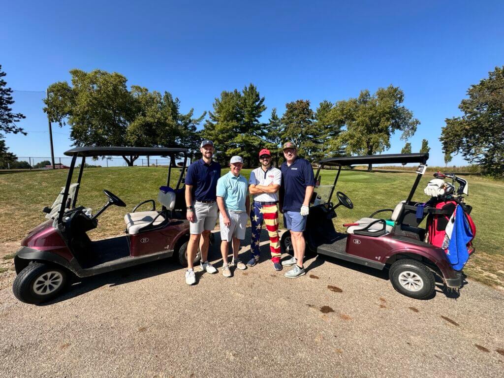 A group of four participants pose with golf carts at the Terry Brewer Memorial Golf Classic