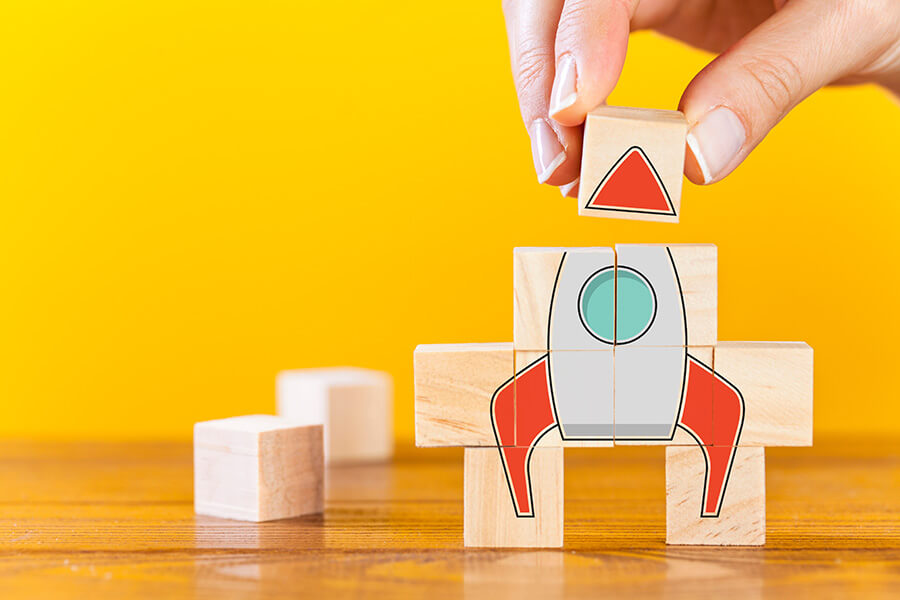Hand arranging wooden cubes in a structure rocket shape.