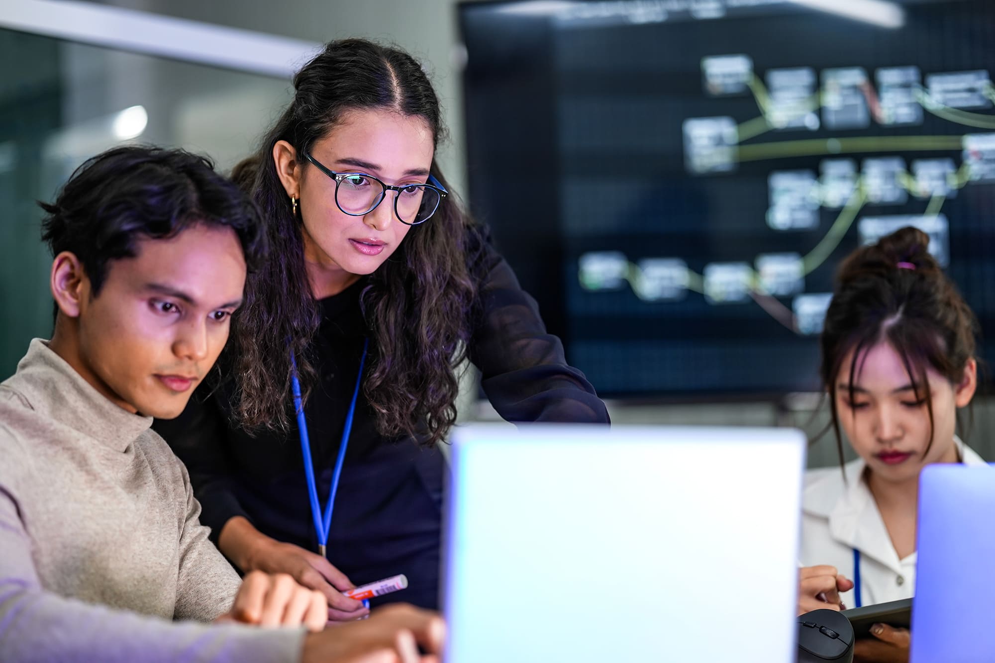 A diverse group of professionals in a corporate workshop on AI d A diverse team of AI developers collaborates on a night coding session. A senior engineer oversees his team, intensely focused on debugging a complex machine learning project.