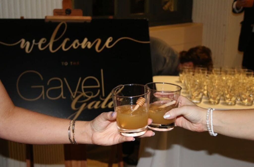 Guests holding drinks in front of a Gavel Gala welcome sign
