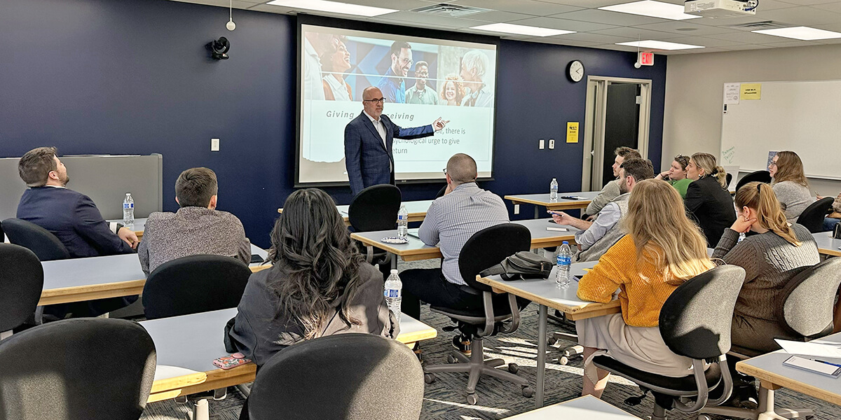YPs - Professional Development Presenter pointing at a screen at the front of a conference room with seated attendees