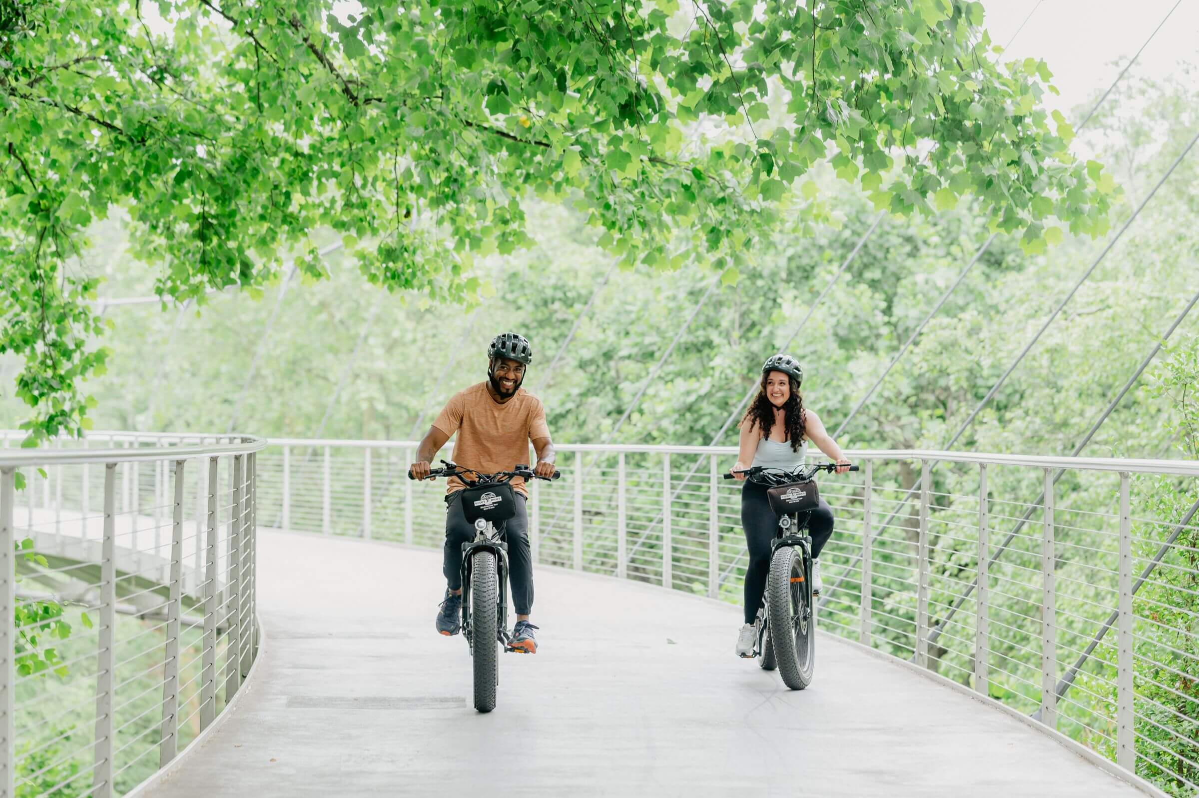 Cyclists riding across an elevated bridge surrounded by green trees