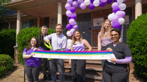 Ribbon cutting at Elevate Audiology under a purple and white balloon arch