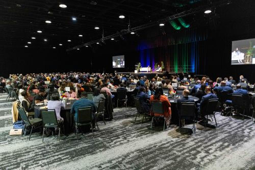 Large audience seated at round tables in a ballroom event