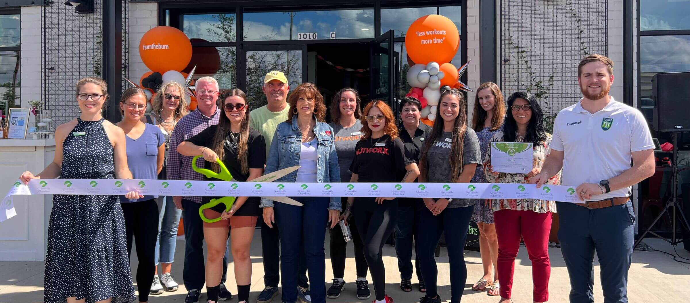 Ribbon cutting celebration outside a storefront with orange balloons